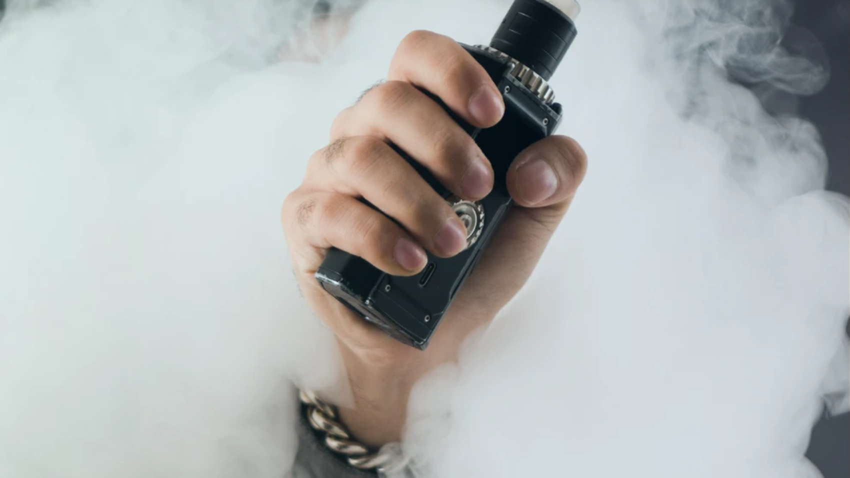 Primer plano de una mano sosteniendo un cigarrillo electrónico rodeado de vapor.