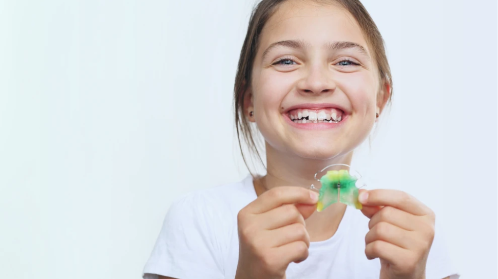 Niña feliz mostrando su aparato dental removible con una gran sonrisa.